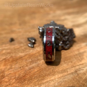 Puede incluir: Un anillo de plata con una incrustación roja y plateada. El anillo está sobre una superficie de madera.