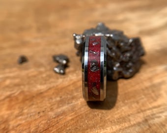 Peut inclure: Une bague en argent avec un incrustation rouge et argent. La bague est sur une surface en bois.