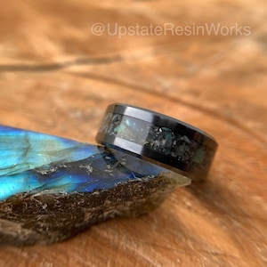 May include: A black tungsten carbide ring with a band of iridescent blue and green abalone shell and black glitter embedded in clear resin.