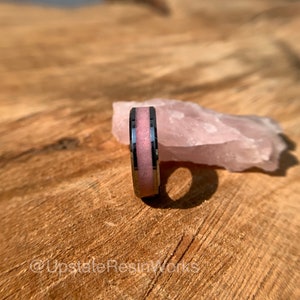 May include: A silver ring with a pink resin inlay. The ring is sitting on a piece of rose quartz.