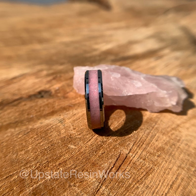 May include: A silver ring with a pink resin inlay. The ring is sitting on a piece of rose quartz.