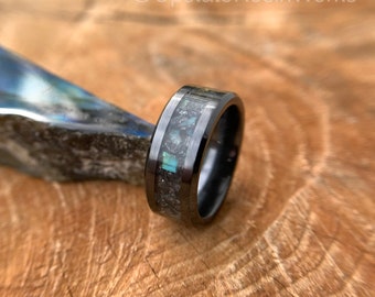 May include: Black tungsten carbide ring with a dark blue and grey inlay. The ring is on a wooden surface.