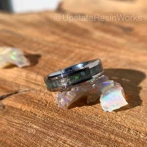 May include: A silver ring with a green and white inlay. The ring is sitting on a piece of iridescent rock.