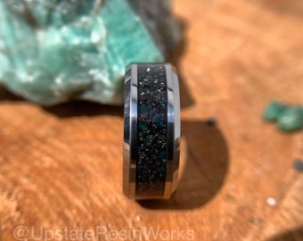 May include: A silver ring with a black and green inlay. The inlay is made of small, sparkly particles.