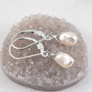 May include: A pair of silver earrings with white pearl drops. The earrings are on a light gray background.