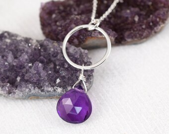 May include: A silver chain necklace with a large, faceted amethyst gemstone pendant. The pendant is attached to a simple silver circle.