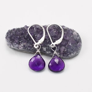 May include: A pair of silver earrings with purple amethyst gemstone drops. The earrings have a simple wire design and are perfect for everyday wear.