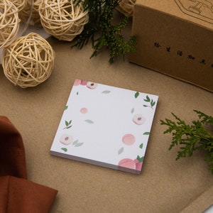 Peut inclure: Un bloc de notes autocollantes blanches avec un motif de fleurs de pêcher. Les notes ont un motif floral rose et vert avec des fleurs de pêcher et des feuilles.