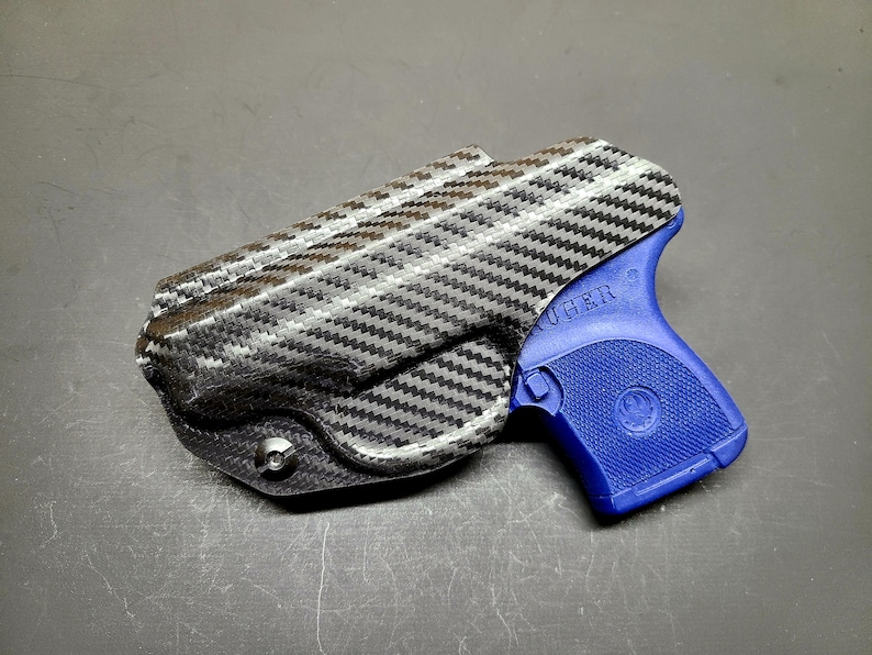 May include: A blue Ruger pistol with a black carbon fiber holster. The holster has a screw on the bottom.