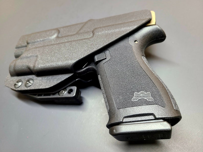 May include: A black polymer handgun with a black polymer holster. The handgun has a black polymer grip with a "PISTOLERA" logo. The holster has a black polymer clip.