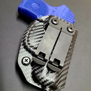 May include: A black carbon fiber holster with a blue polymer handgun inside. The holster has a metal clip with screws.