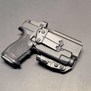 May include: A black handgun with a black holster and a red dot sight. The holster has a clip for attaching to a belt.