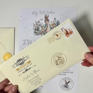 May include: A cream-colored envelope with a gold wax seal and a decorative stamp featuring a bunny rabbit. The envelope is addressed to Amelia Williams with a street address, city, and postal code. The text "Easter Delivery" is printed on the envelope.