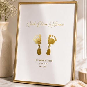 May include: A framed print with gold foil lettering and footprints. The text reads "Noah Oliver Williams", "13th March 2025", "7:18 AM", and "7lb 2oz". The frame is gold and the background is white.