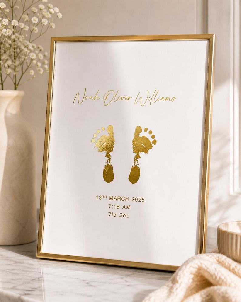 May include: A framed print with gold foil lettering and footprints. The text reads "Noah Oliver Williams", "13th March 2025", "7:18 AM", and "7lb 2oz". The frame is gold and the background is white.
