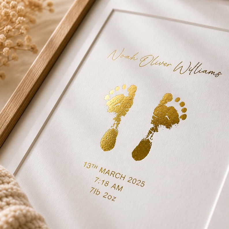 May include: A framed print featuring two gold-colored baby footprints. The print includes the name "Noah Oliver Williams", the date "13th March 2025", time "7:18 AM", and weight "7lb 2oz". The frame is light-colored wood.