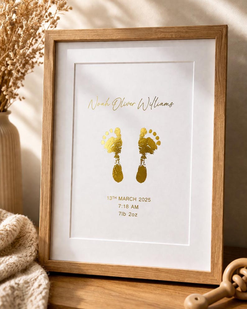 Op de afbeelding: Een ingelijste print met een licht houten frame. De print toont gouden voetstappen, de naam "Noah Oliver Williams" en geboortegegevens: 13 maart 2025, 7:18 uur, en 3,2 kg.