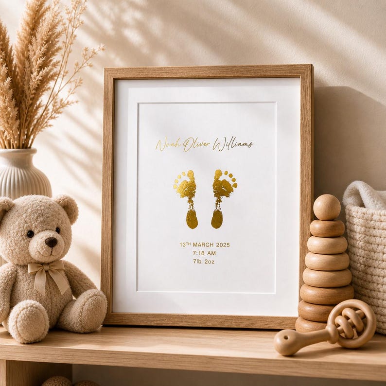 May include: A framed print with a baby's footprints in gold foil. The print includes the baby's name, birth date, time, and weight. The frame is light brown, and the print is displayed on a wooden shelf with a teddy bear and other baby items.