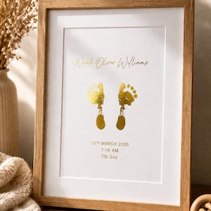 May include: A framed print with a light wood frame. The print features gold foil footprints, the name "Noah Oliver Williams", and birth details: March 13, 2025, 7:18 AM, and 7lb 2oz.