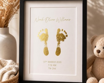Puede incluir: Una impresión enmarcada en negro con huellas de pies de bebé en lámina dorada en el centro. El texto dice Noah Oliver Williams, 13th March 2025, 7:18 AM y 7lb 2oz. El diseño está sobre un fondo blanco en un marco rectangular sencillo.