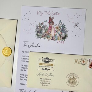 May include: A white card with a watercolor illustration of a bunny rabbit surrounded by flowers and eggs. The card says "My First Easter" and "To Amelia" with the year 2025. The card is part of an Easter delivery package.