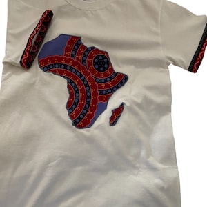 Peut inclure: T-shirt blanc avec une applique en forme de continent africain à motifs bleus et rouges. L'applique est bordée de blanc et est centrée sur le t-shirt. Le t-shirt porte une étiquette Gildan sur le devant.