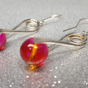 Oorbellen van rode glaskralen (lengte 3,5 cm) bestaande uit 10 mm rode glaskralen opgehangen tussen twee gedraaide metalen staven.