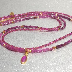 Könnte beinhalten: Eine mehrreihige Halskette aus kleinen, facettierten rosa Edelsteinen und goldenen Akzenten. Die Halskette hat einen Anhänger mit einem tropfenförmigen rosa Edelstein. Der Schmuck wird auf einer silbernen Oberfläche präsentiert.
