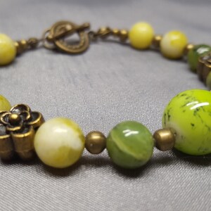 May include: A green and yellow beaded bracelet with bronze flower accents and a bronze clasp.