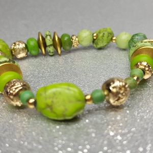 Pulsera flexible* de 20 cm en color verde realizada con piedras de howlita de varias formas y tamaños, cuentas de metal color dorado con elementos decorativos.
