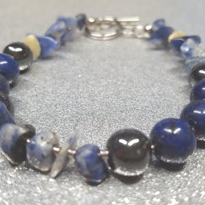 Pulsera* de lapislázuli (20 cm de largo) con cuentas de 8 mm y elementos metálicos decorativos. Cierre de palanca metálico.