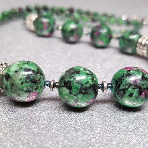 Op de afbeelding: Een groene en roze edelsteen ketting met zilveren kralen. De ketting is gemaakt van ronde, gefacetteerde kralen.