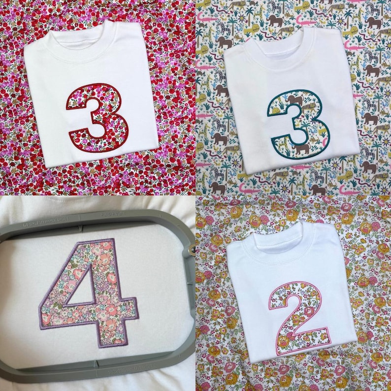 May include: A collection of white t-shirts featuring embroidered numbers on the front. The numbers are filled with various floral and animal patterns, including a red floral three, a jungle animal three, a floral four in a hoop, and a floral two.