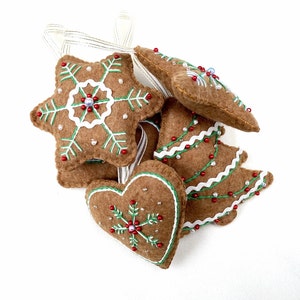 May include: Five felt Christmas ornaments shaped like a star, heart, and Christmas tree. The ornaments are brown with green and white embroidery and red and white beads.