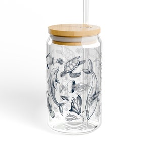 May include: A clear glass reusable drinking cup with a bamboo lid and a glass straw. The cup has a design of sea creatures including a whale, dolphin, turtle, and jellyfish.