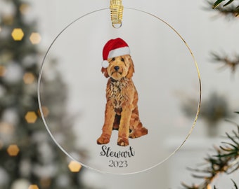 Könnte beinhalten: Runder Weihnachtsbaumschmuck aus Glas mit einem braunen und weißen Hund, der eine rote Weihnachtsmütze trägt. Der Schmuck ist mit dem Namen "Stewart" und dem Jahr "2023" bedruckt.
