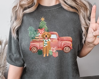 May include: A dark gray t-shirt with a Christmas-themed design featuring a red truck carrying a Christmas tree and a golden retriever dog wearing a green scarf.