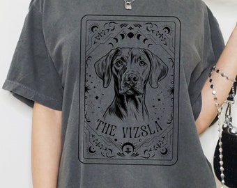 May include: A gray oversized t-shirt with a black graphic of a dog's head in a tarot card style frame. The text "The Vizsla" is printed below the dog's head.