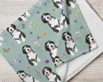 May include: A soft, plush throw blanket featuring a repeating pattern of black and white dogs with a light green background. The dogs are surrounded by colorful flowers and butterflies.
