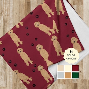 May include: A red fleece blanket with a repeating pattern of golden doodle dogs and black paw prints. The blanket has a white border and a white backing. The image also shows six colour options for the blanket.