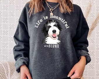 Puede incluir: Una sudadera gris oscuro con el texto "Life is Beautiful with Bernie" y una imagen de dibujos animados de un perro blanco y negro.