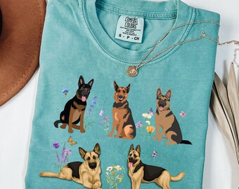 Puede incluir: Camiseta verde espuma de mar con un gráfico de cinco pastores alemanes, flores y mariposas. La camiseta tiene una etiqueta Comfort Colors y un collar dorado. La palabra "Seafoam" está impresa en la parte superior.