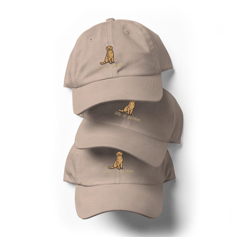 May include: Three tan baseball caps stacked on top of each other. Each cap has a small embroidered image of a golden retriever dog and the phrase "life is golden" in a matching tan color.