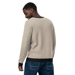 May include: A beige long-sleeve sweater with a black ribbed collar and cuffs. The sweater is made of a soft, comfortable material.