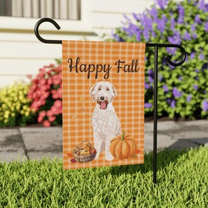May include: A garden flag on a black metal stand. The flag displays a white dog, a pumpkin, and a basket of gourds against an orange and white checked background. The words "Happy Fall" are printed at the top.