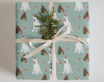 May include: Wrapped gift with light green wrapping paper featuring a repeating pattern of white dogs with antlers, Christmas trees, and gold stars. The gift is tied with a cream-colored ribbon and a sprig of greenery.