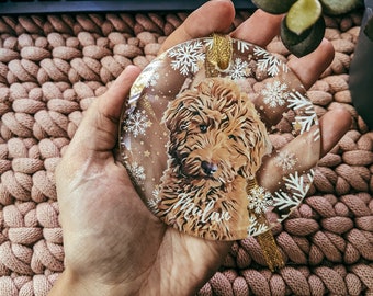 Könnte beinhalten: Ein transparenter Weihnachtsbaumschmuck aus Glas mit einem goldenen Band und einem braunen und weißen Hund im Inneren. Der Name des Hundes ist "Milan" auf den Baumschmuck gedruckt.