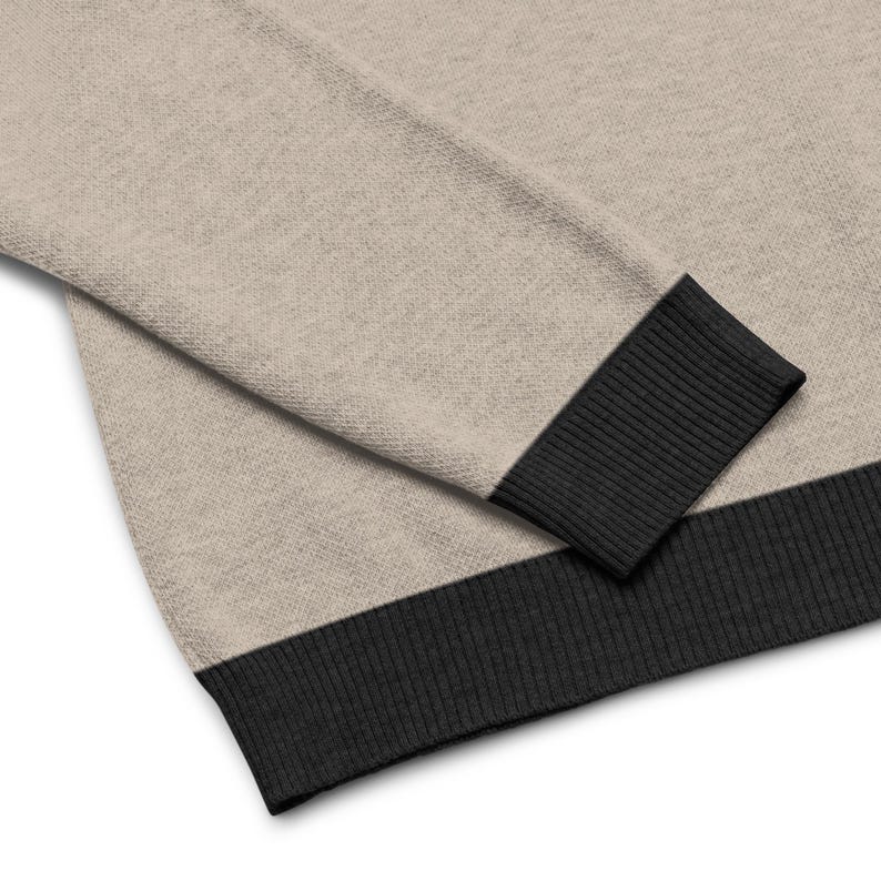 May include: A beige sweater with a black ribbed trim around the cuffs and bottom hem.