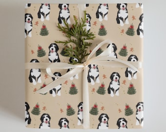 Puede incluir: Regalo envuelto con un fondo beige con un patrón repetido de perros blancos y negros, árboles de Navidad y hombres de jengibre. Una ramita de vegetación y una cinta color crema con un lazo adornan el paquete.