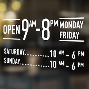 Op de afbeelding: Een wit bord met zwarte tekst op een wazige achtergrond. Het bord zegt "OPEN 9AM-8PM MONDAY-FRIDAY" en "SATURDAY...10 AM - 6 PM" en "SUNDAY...10 AM - 6 PM".